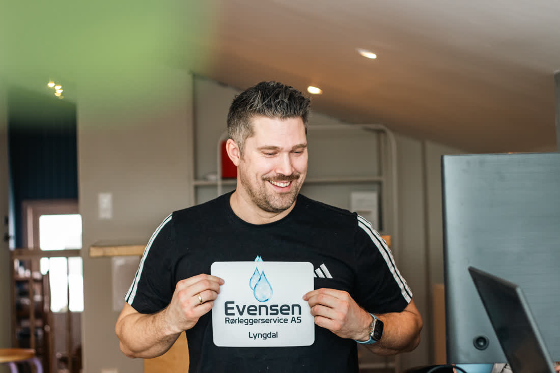 Jonas Evensen holder opp Evensen Rørleggerservice-skilt i Lyngdal